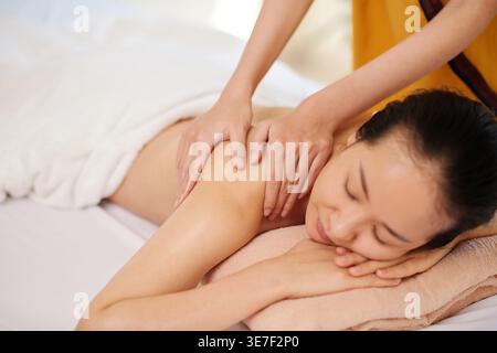 Femme asiatique avec les yeux fermés obtenant le massage de retour couché sur le lit dans le spa Banque D'Images