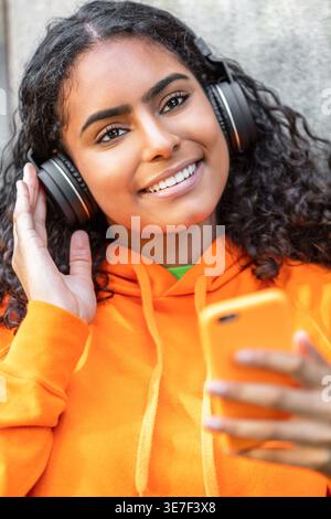 Femme noire souriante écoutant de la musique avec des écouteurs debout à l'extérieur Banque D'Images