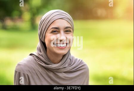 Femme arabe joyeuse portant le hijab assis dans le parc pendant la journée Banque D'Images