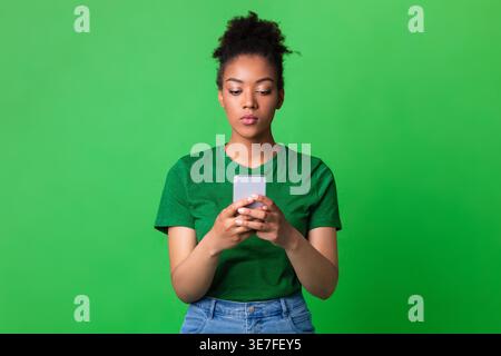 Femme noire utilisant un smartphone debout sur fond vert en studio Banque D'Images