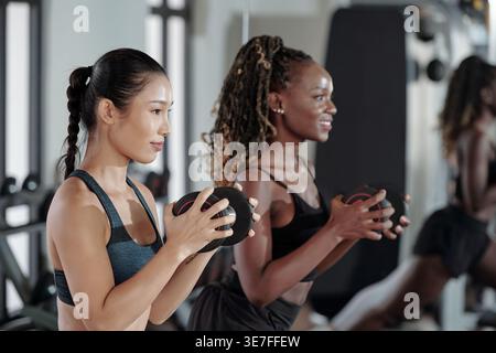 Amies asiatiques et noires faisant des fentes avec des haltères dans le gymnase Banque D'Images