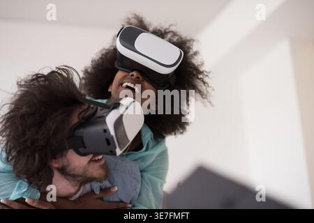 Couple noir et caucasien portant des casques VR ayant un plaisir piggyback équitation et expérimentant la réalité virtuelle sur fond blanc en studio Banque D'Images