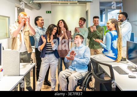 Équipe d'affaires diversifiée applaudissant et célébrant le succès dans un bureau moderne avec un collègue handicapé Banque D'Images