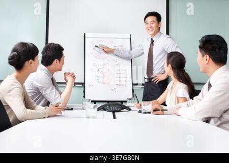 Homme d'affaires chinois souriant debout et présentant le plan d'affaires menant la réunion d'équipe dans le bureau Banque D'Images
