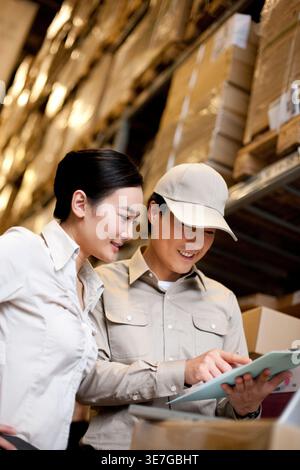 Travailleur chinois masculin et féminin tenant une planche à pince vérifiant les stocks debout dans l'entrepôt Banque D'Images