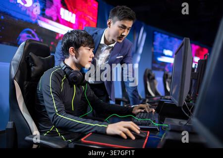 Homme chinois sérieux entraînant des joueurs masculins jouant à l'esport sur ordinateur dans l'arène Banque D'Images