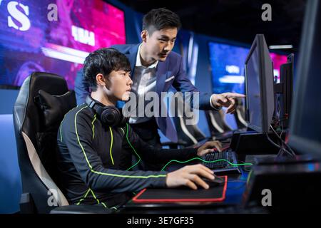 Homme chinois sérieux entraînant des joueurs masculins jouant à l'esport sur ordinateur dans l'arène Banque D'Images
