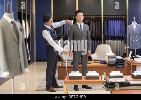 Concepteurs de mode masculins chinois seniors prenant la mesure du client masculin chinois tout en se tenant dans la boutique de mode Banque D'Images
