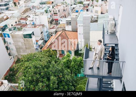 Collègues d'affaires femmes asiatiques et hommes caucasiens debout sur l'escalier de secours regardant la vue sur la ville pendant la pause-café Banque D'Images