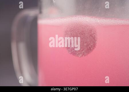 Comprimé effervescent se dissolvant dans une tasse en verre d'eau rose gros plan réaction de boisson fraîche Fizzy Banque D'Images