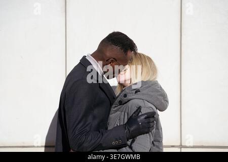 Couple noir et caucasien embrassant debout contre le mur le jour ensoleillé Banque D'Images