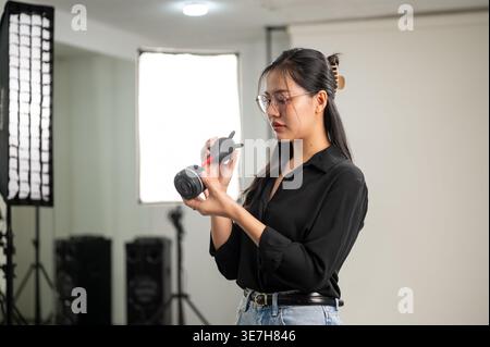 Objectif d'appareil photo de nettoyage de photographe asiatique sérieuse debout sur le côté sur fond blanc en studio Banque D'Images