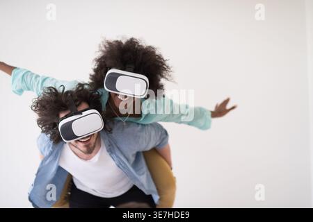 Couple noir et caucasien portant des casques VR ayant un plaisir piggyback équitation et expérimentant la réalité virtuelle sur fond blanc en studio Banque D'Images