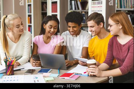 Souriant Noir étudiant d'université utilisant un ordinateur portable avec ses amis à table dans la bibliothèque Banque D'Images
