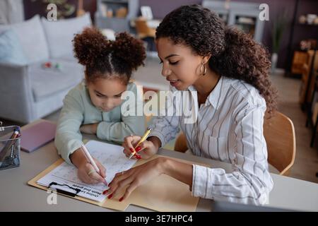 Fille métisse faisant ses devoirs avec sa mère lui enseignant à la maison Banque D'Images