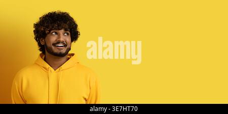 Homme asiatique regardant loin debout sur fond jaune dans le studio Banque D'Images