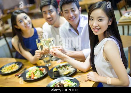 Joyeux amis asiatiques, hommes et femmes, assis à table, à prendre des verres de champagne et à dîner ensemble au restaurant Banque D'Images