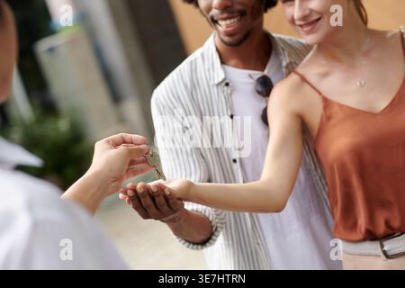 Agent immobilier masculin asiatique donnant les clés de la maison à un couple noir et caucasien debout à l'extérieur pendant la journée Banque D'Images