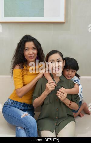 Grand-mère asiatique embrassée par sa fille et sa petite-fille assis sur le canapé ensemble à la maison Banque D'Images