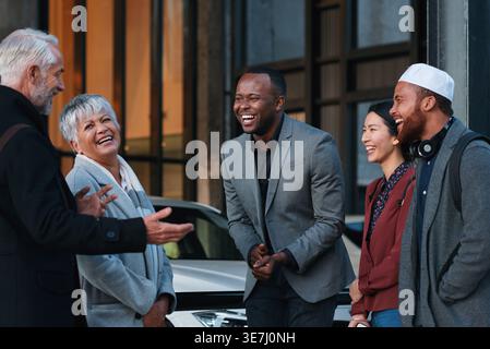 Heureux, les gens d'affaires et rire avec l'équipe pour blague drôle, humour ou comédie ensemble dans la ville. Diversité, groupe ou collègues parlant avec sourire pour Banque D'Images