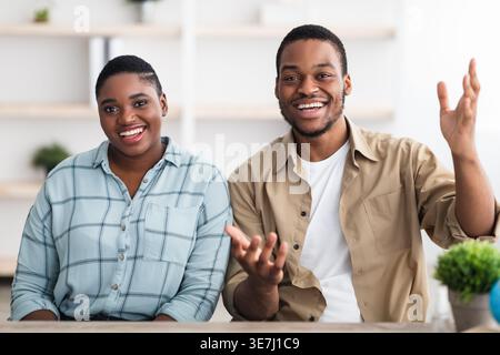 Joyeux couple noir parlant et faisant des gestes tout en étant assis à la table en bois à la maison Banque D'Images