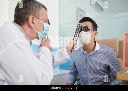 Homme asiatique assis portant des lunettes réglables tandis que le médecin caucasien le vérifiant à la clinique Banque D'Images