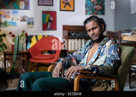 Artiste masculin indien sérieux assis dans un fauteuil se relaxant dans un studio d'art pendant la journée Banque D'Images