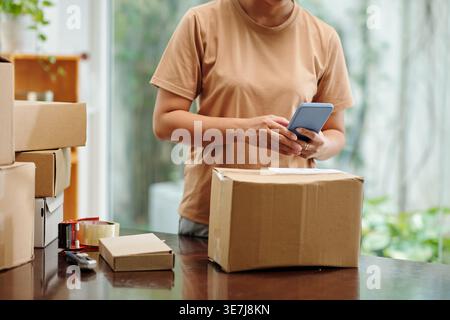 Femme asiatique tenant un smartphone debout avec des paquets de boîte sur la table à la maison Banque D'Images
