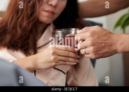Mari asiatique donnant tasse de tisane à la femme malade se reposant sur le lit à la maison Banque D'Images