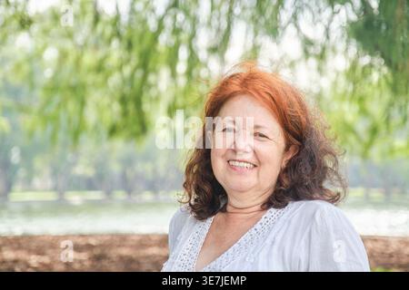 Femme hispanique senior en robe blanche assise dans le parc pendant la journée Banque D'Images