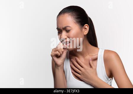 Femme asiatique touchant sa poitrine souffrant de douleur toux tout en se tenant debout sur fond blanc dans le studio Banque D'Images