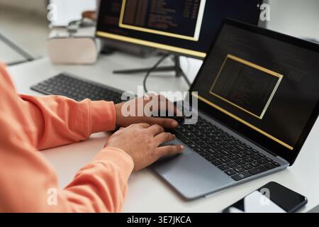 Mains de programmeur féminin mixte travaillant des codes sur ordinateur portable tout en étant assis à table avec ordinateur dans le bureau Banque D'Images