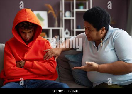 Mère noire parlant à son fils adolescent portant un sweat à capuche tout en étant assis sur un canapé dans le salon à la maison Banque D'Images
