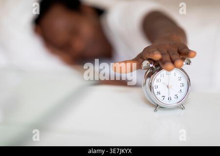 Mains de l'homme noir éteignant le réveil sur la table de chevet tout en étant allongé sur le lit à la maison Banque D'Images