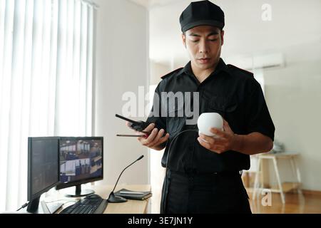 Garde de sécurité masculin asiatique tenant du matériel de surveillance debout à table près de l'ordinateur dans le bureau de sécurité Banque D'Images