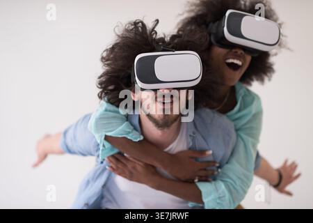 Couple noir et caucasien portant des casques VR ayant un plaisir piggyback équitation et expérimentant la réalité virtuelle sur fond blanc en studio Banque D'Images