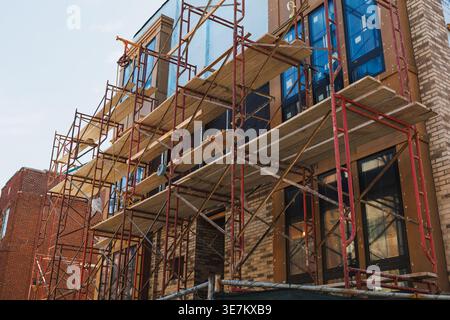Les équipes de construction utilisent des échafaudages pour accéder aux parties supérieures d’un bâtiment en cours de rénovation. Outils et matériaux sont dispersés autour du site Banque D'Images
