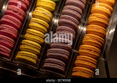 Rangées de macarons colorés dans une vitrine de boulangerie. Assortiment de pâtisseries françaises en rose, jaune, violet et orange, concept de confiserie, bonbons, des Banque D'Images