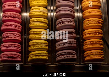 Rangées de macarons colorés dans une vitrine de boulangerie. Assortiment de pâtisseries françaises en rose, jaune, violet et orange, concept de confiserie, bonbons, des Banque D'Images