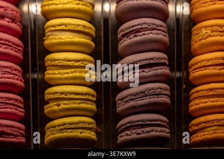 Rangées de macarons colorés dans une vitrine de boulangerie. Assortiment de pâtisseries françaises en rose, jaune, violet et orange, concept de confiserie, bonbons, des Banque D'Images