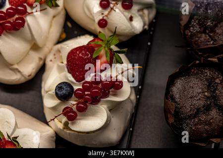 Gros plan d'un dessert meringue garni de fraises fraîches, de groseilles rouges et de myrtilles. Pâtisserie sucrée sur l'affichage avec muffins en arrière-plan, concept de Banque D'Images