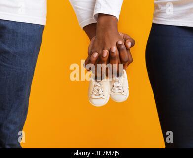 Couple noir tenant des bottes de bébé debout sur fond jaune dans le studio Banque D'Images