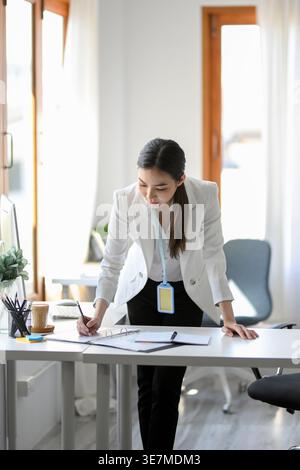 Femme d'affaires asiatique appuyée sur la table écrivant des notes dans le bureau pendant la journée Banque D'Images