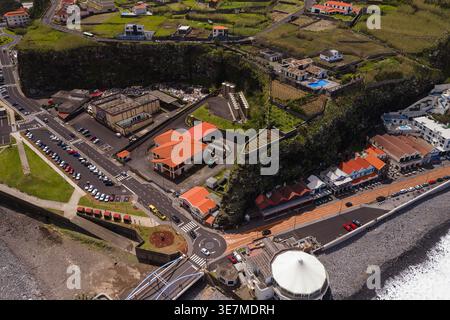 Vue aérienne d'a Madère, village portugais avec falaise de basalte, champs en terrasses, toits de tuiles rouges, route en bord de mer, rond-point, toit circulaire blanc, galets Banque D'Images