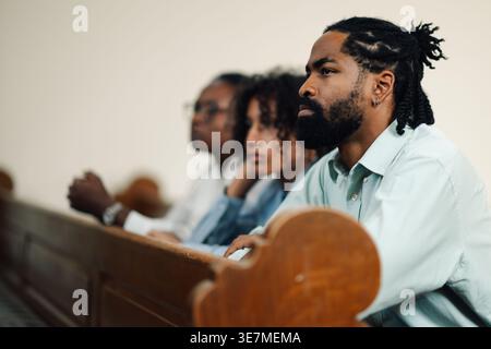 Homme noir avec moustache et barbe assis sur un banc en bois avec sa femme et son fils assistant à la messe à l'église Banque D'Images