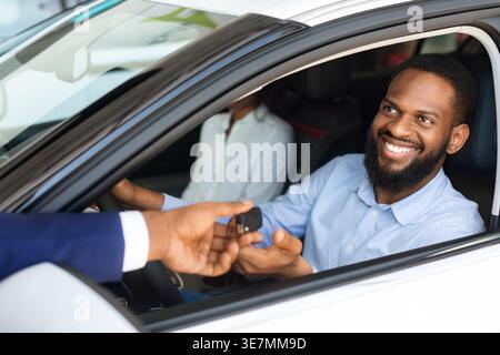 Homme noir avec la barbe prenant les clés de voiture d'auto du vendeur tout en étant assis à côté de wifein voiture à la salle d'exposition Banque D'Images
