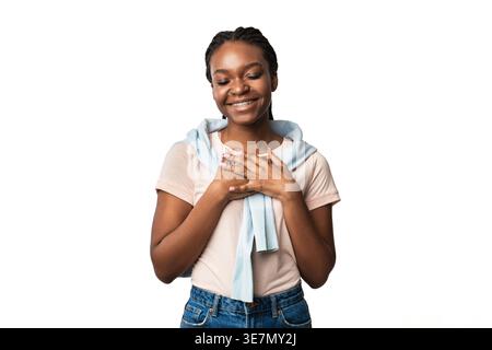 Femme noire souriante avec des appareils dentaires pressant les mains à la poitrine debout avec les yeux fermés sur fond blanc dans le studio Banque D'Images