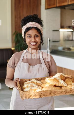 Femme mixte portant un tablier tenant un plateau de pâtisserie tout en se tenant debout dans la boulangerie Banque D'Images
