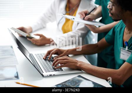 Infirmière noire tapant sur un ordinateur portable assis à côté de collègues prenant des notes dans la salle de conférence de l'hôpital Banque D'Images
