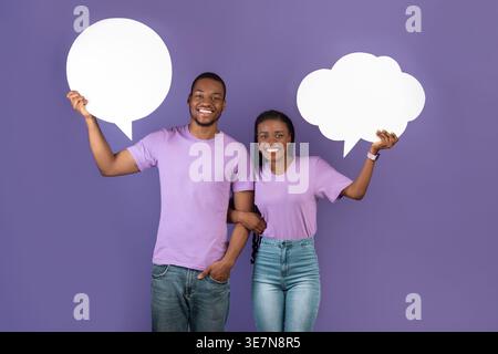Sourire couple noir tenant des bulles de parole tout en se tenant debout sur fond violet dans le studio Banque D'Images
